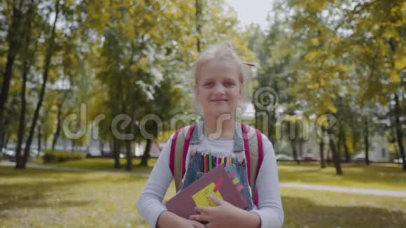 快乐的女学生带着背包拿着一本书住在学校院子里一个漂亮聪明的女孩微笑的肖像视频的预览图