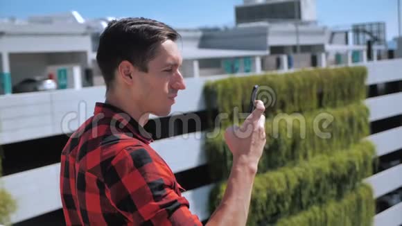 有魅力的男人穿着格子衬衫在城市背景下在户外使用智能手机触摸屏幕设备人员和视频的预览图