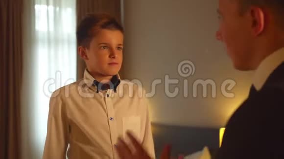男孩在旅馆房间给男人系上领带父亲和儿子说话视频的预览图