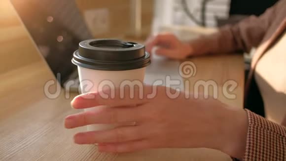 专注于咖啡杯女性在阳光明媚的日子里喝咖啡在笔记本电脑上工作视频的预览图