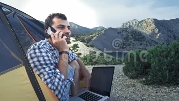 自由职业者使用笔记本电脑工作坐在海滩上的露营帐篷里在电话里说话自由职业者视频的预览图