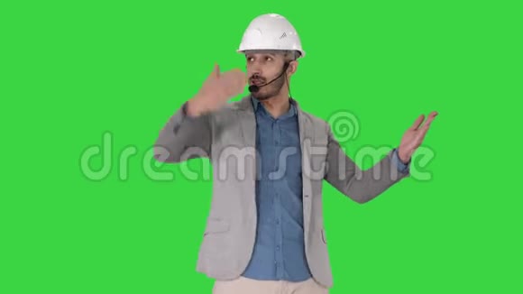 戴着头盔和头部的建筑师与摄像机交谈并在绿色屏幕上显示一些物体的手势视频的预览图