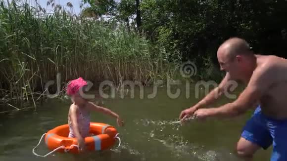 父女俩泼水救生圈里有泳衣和头巾的女孩视频的预览图