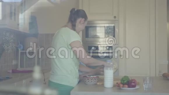 侧面看着年轻女子和她的小女儿在家厨房里做蛋糕女孩和母亲混合面粉视频的预览图