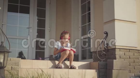 暑假期间可爱的女孩坐在房子附近的院子里听音乐唱歌看书视频的预览图