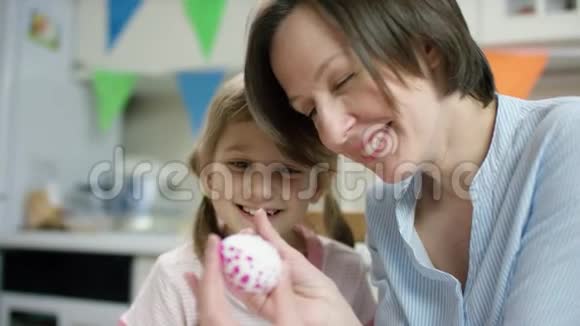 母亲和女儿坐在餐桌旁一起用彩蛋做窝子并互相拥抱视频的预览图