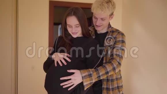 快乐的青少年夫妇站在家里在一起那个年轻人抚摸着怀孕女朋友的肚子未成年人视频的预览图