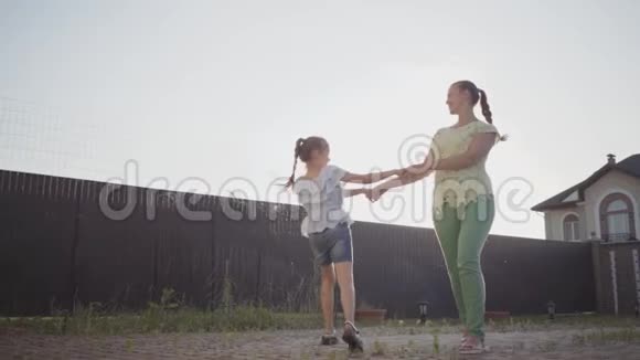 快乐的小可爱女孩和她的母亲在后院里牵着手旋转女人和孩子玩得开心视频的预览图