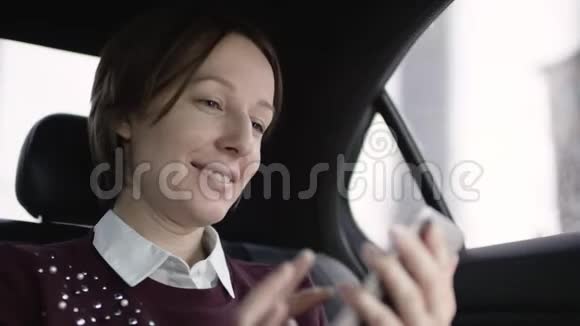 穿着白色衬衫和栗色毛衣的棕色头发的女人坐在车里微笑着输入信息视频的预览图