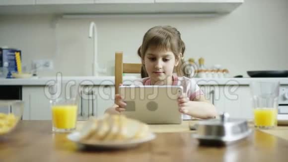 高兴的女孩坐在桌子旁手里拿着平板电脑等着其他家人吃午饭视频的预览图