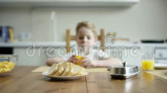 一个可爱的男孩拿着一杯橙汁坐在桌旁等着另一家人吃一顿超量照相机视频的预览图