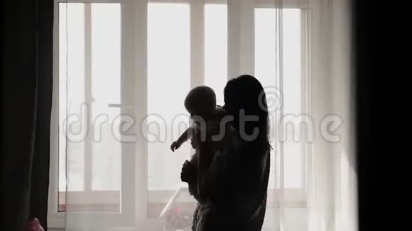 窗户附近的年轻美丽母亲和小女孩剪影视频的预览图