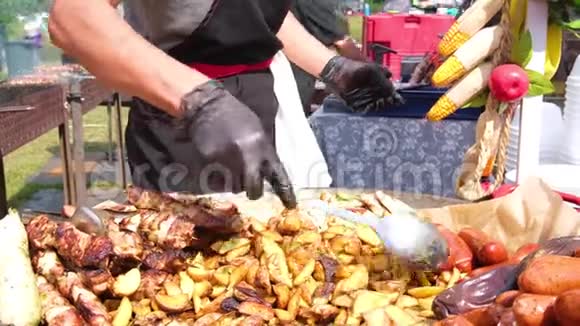 街头美食节一位穿着黑色衣服和手套的厨师增加了一批新土豆土豆烤香肠肉视频的预览图