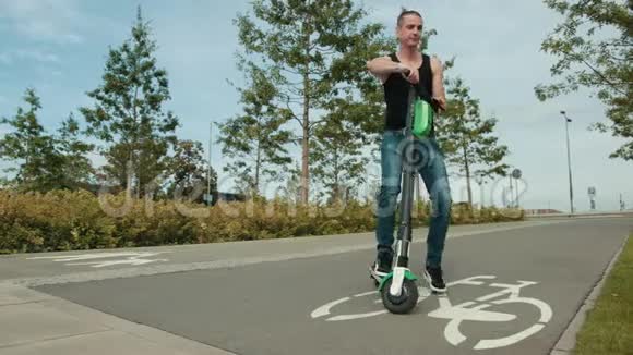 穿着黑色衣服和牛仔裤的男人骑着电动滑板车在城市里转悠视频的预览图