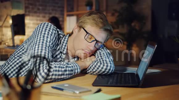 一张疲惫的男人晚上睡在黑暗办公室的书桌上躺在书桌上的画像视频的预览图
