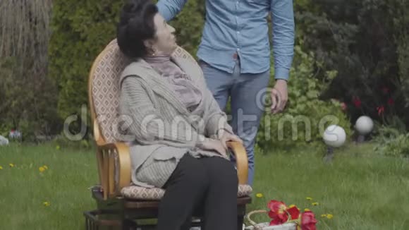 肖像成熟的女人坐在摇椅上享受阳光成年孙子过来拥抱这个女人视频的预览图