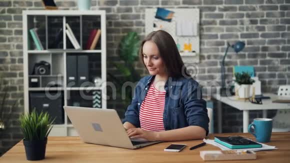 开朗的女孩在办公室使用笔记本电脑后在工作中微笑放松视频的预览图