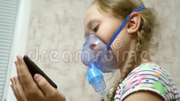 一个戴着面具的生病女孩吸入一个喷雾瓶在平板电脑上玩电脑游戏戴着蓝色医院面具的孩子视频的预览图