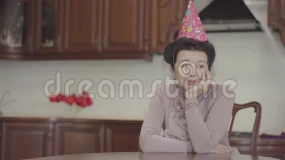 成熟的女士坐在桌边头上戴着生日帽成年孙子带来小蛋糕穿上视频的预览图