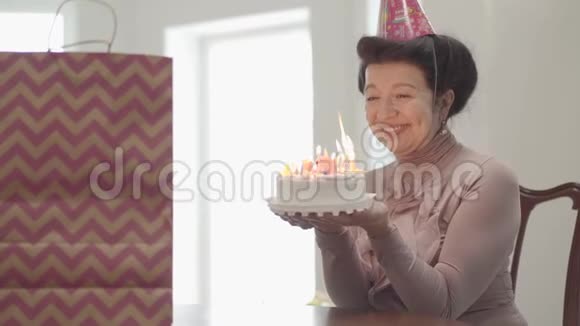 肖像情感微笑的女士坐在桌边拿着许多蜡烛的小蛋糕成年孙子拥抱视频的预览图
