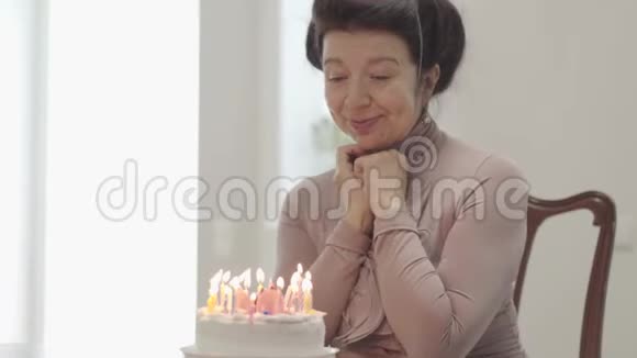 肖像奶奶坐在桌子前的小蛋糕上有许多蜡烛成年孙子拥抱女人视频的预览图