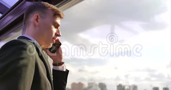 商人的电话交谈一个年轻人穿着灰色西装站在靠近窗户的办公室里打电话视频的预览图