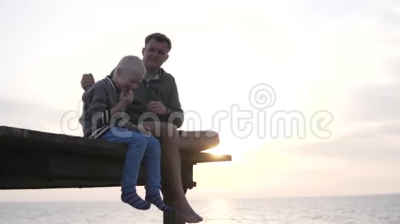 爸爸和儿子在一边聊天一边看着大海上的日落视频的预览图