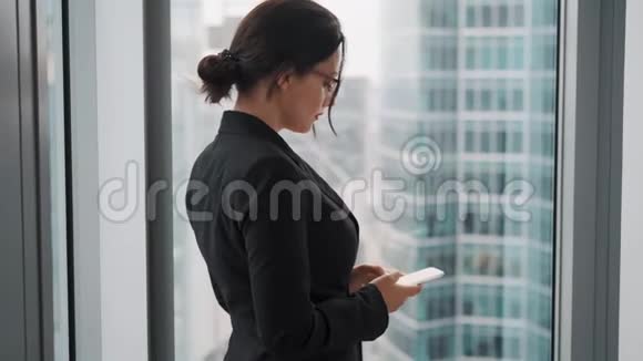 有智能手机的商人肖像穿商务服的女人站在一扇大窗户旁边背景是视频的预览图