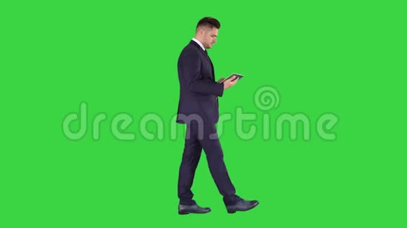 优雅的年轻商人使用他的电脑平板电脑而走在绿色屏幕Chroma键视频的预览图