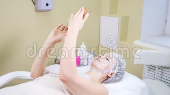 女人在做美容手术时用手机戴上口罩清洗脸部的中间疗法视频的预览图