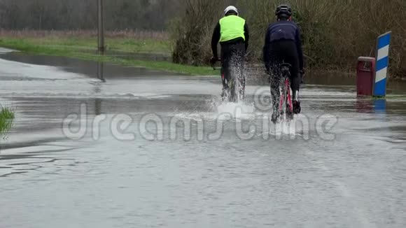 骑自行车的人骑在一条被洪水淹没的道路上水在道路上道路被河流的溢流淹没视频的预览图