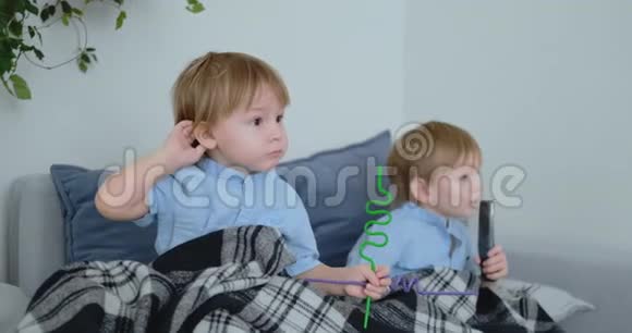 两个男孩4岁和2岁坐在沙发上看电视令人兴奋的电视节目看动画片孩子们看着视频的预览图