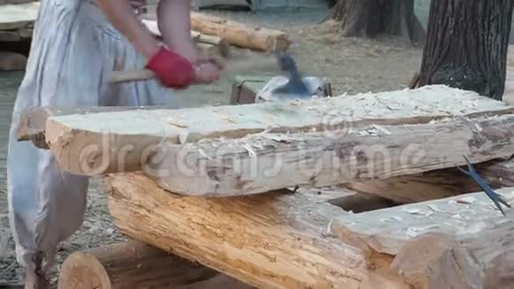 木匠穿着中世纪的棉衣用斧头和硬木一起工作一个人用斧头手工切割木板视频的预览图