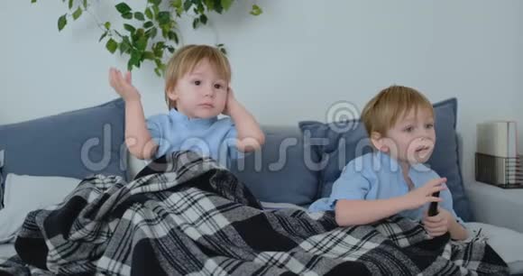 两个男孩4岁和2岁坐在沙发上看电视令人兴奋的电视节目观看漫画视频的预览图