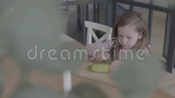 有趣的小女孩坐在桌子旁的椅子上切着西葫芦帮妈妈做饭适当的养育方式视频的预览图