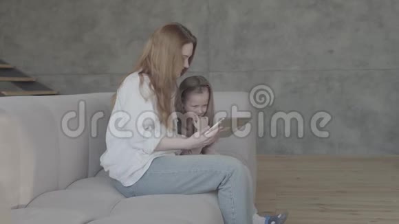 一位年轻的母亲和小女儿长发一起坐在客厅的沙发上用平板电脑这就是视频的预览图