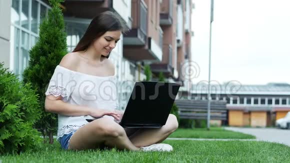快乐的女学生在校园里坐在草地上的笔记本电脑上工作视频的预览图