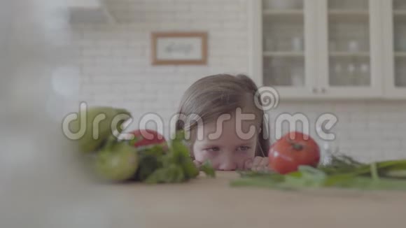 肖像可爱可爱的小女孩从桌子上看躲在镜头里新鲜蔬菜西葫芦视频的预览图