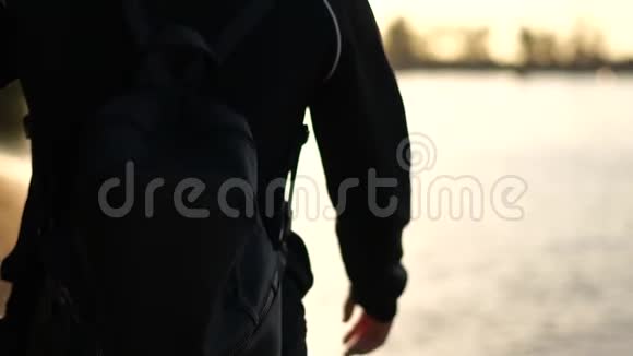 日出时一个穿着黑色运动服背着黑色背包的女孩沿着湖边散步视频的预览图