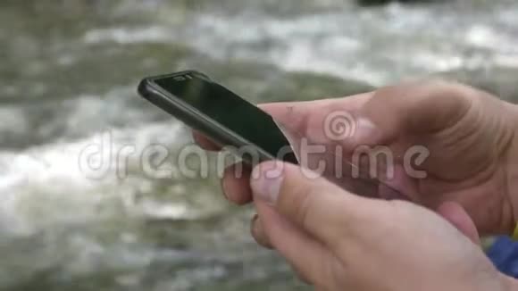 在山溪背景下使用智能手机的无法辨认的男性旅行手视频的预览图