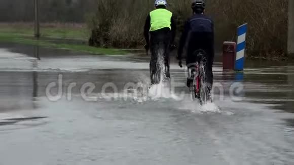 骑自行车的人骑在一条被洪水淹没的道路上水在道路上道路被河流的溢流淹没视频的预览图