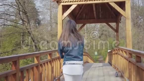 后景年轻迷人的女人慢慢走在木桥上环顾四周女孩欣赏美丽视频的预览图