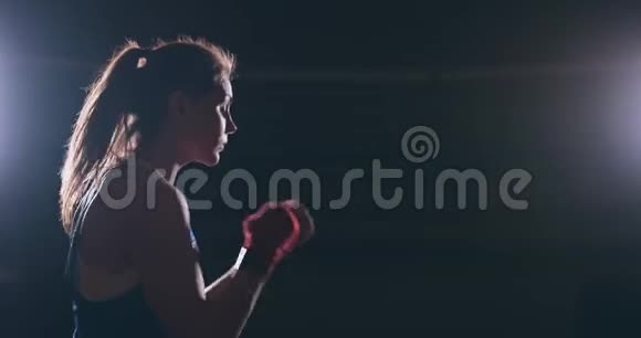 一位身穿红色绷带蓝色t恤的漂亮运动拳手女子正在与一个正在练习拳击的影子搏斗视频的预览图