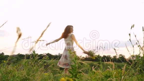 喜笑颜开的姑娘野花盛开花束在傍晚的草地上飞舞视频的预览图