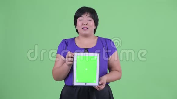 一位年轻体重超重的亚洲女性一边说一边展示数字平板电脑视频的预览图