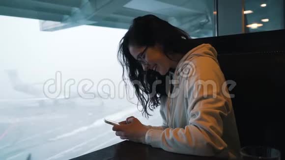 有智能手机的女孩坐在机场候机楼里视频的预览图