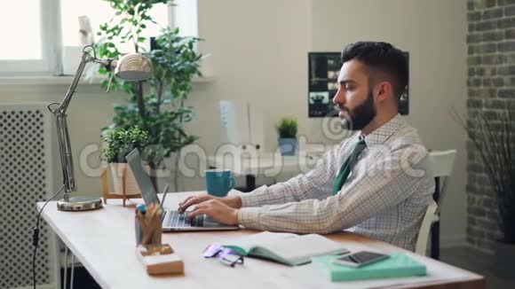 有胡子的人用笔记本电脑工作然后伸展手臂放松办公室视频的预览图