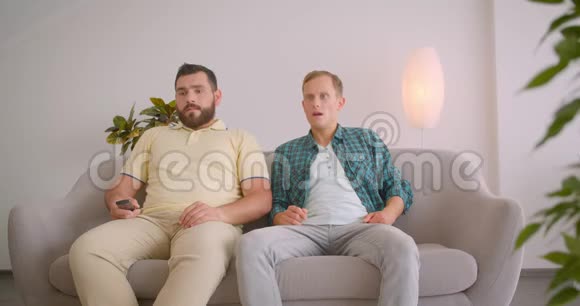 两个在电视上看足球的白人男子因在家中坐在沙发上迷了路而心烦意乱视频的预览图