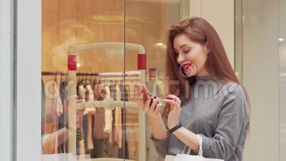 可爱的年轻女子笑着在商场购物时用智能手机视频的预览图