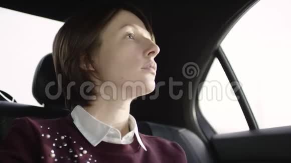 穿着白色上衣和栗色毛衣的棕色头发的漂亮女人坐在车里看着窗户视频的预览图
